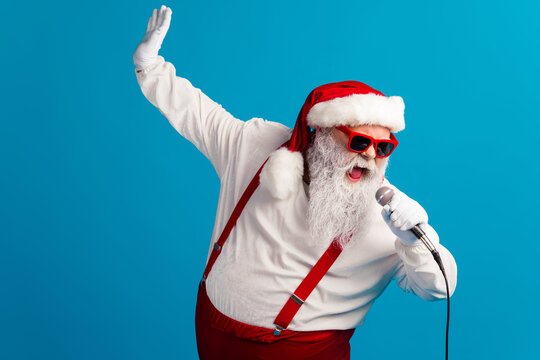 Santa with red suspenders and hat sings into a microphone in a fun festive scene against a bright blue background for Christmas joy and holiday shopping inspiration