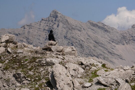 Un homme seul v&ecirc;tu de noir, assis sur un rocher en montagne, en train de r&eacute;fl&eacute;chir, d'admirer l'immensit&eacute; de la nature qui l'entoure