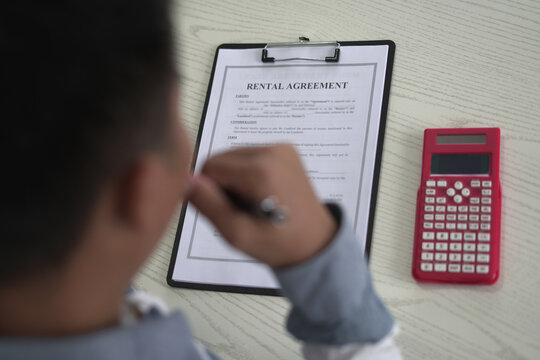 A real estate male agent is reading and checking paper documents, signing the lease agreement, preparing contract and terms and conditions details and checking data analysis as a remote freelancer.