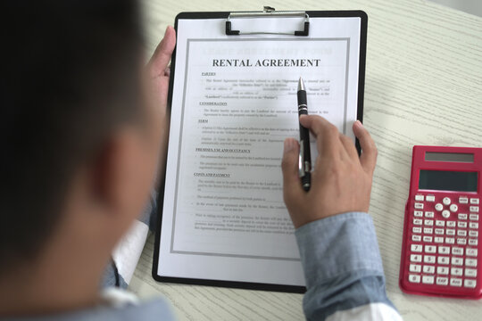 A real estate male agent is reading and checking paper documents, signing the lease agreement, preparing contract and terms and conditions details and checking data analysis as a remote freelancer.