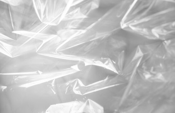 Abstract close-up of a crinkled transparent plastic surface in black and white tones with soft lighting and shadows.