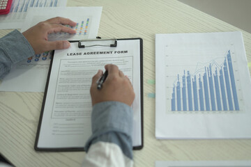 A real estate male agent is reading and checking paper documents, signing the lease agreement, preparing contract and terms and conditions details and checking data analysis as a remote freelancer.