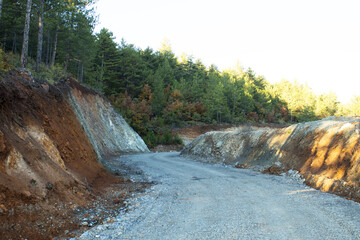 Unpaved gravel road in a hillside cutting within a forested mountain area, showing earthworks and rural infrastructure.