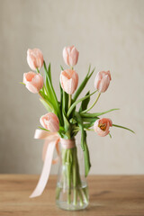 A bouquet of delicate pink tulips in a glass vase on a wooden table.