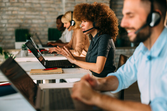 Engaged female customer service agent actively communicates with expressive hand gestures while working on a laptop in a modern, diverse call cente