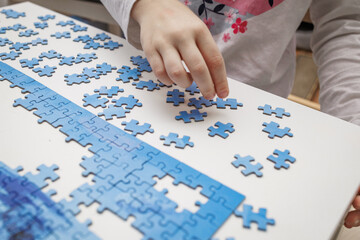 Close-up of a child’s hand arranging puzzle pieces on a white table. Symbol of creativity, focus, and early learning through play