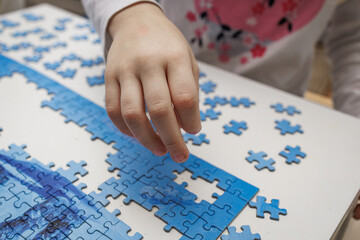 Close-up of a child’s hand assembling a blue jigsaw puzzle. Symbol of focus, learning, and early...