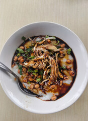 Bowl of savory chicken congee topped with herbs, peanuts, and a drizzle of soy sauce