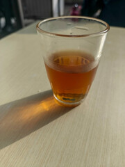 Amber-hued beverage in a clear glass casting a long shadow on a light-colored wooden surface