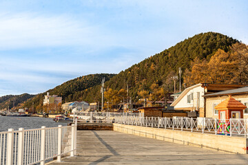 Autumn Promenade along Lake Baikal and surrounding mountains by Listvyanka Village with waterfront Boats, hillside Town, along Shoreline and Colorful Trees