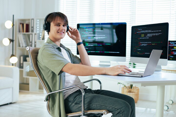Smiling programmer in headphones working on laptop at white table in office