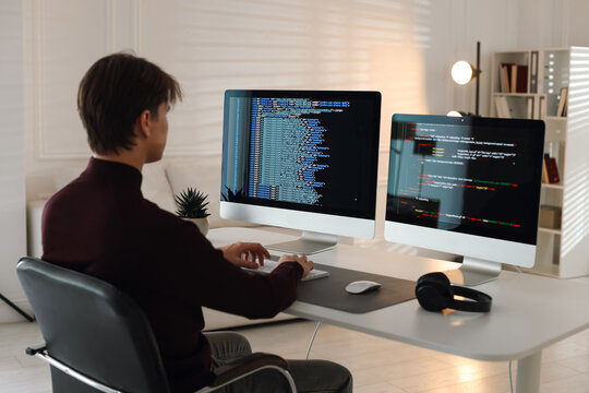 Programmer working on computer with dual monitors at white table in office