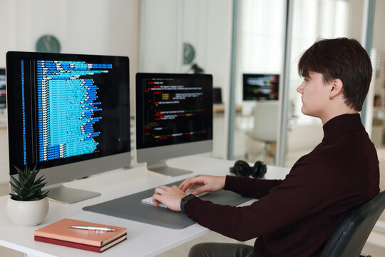 Programmer working on computer with dual monitors at white table in office