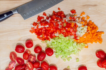 Fresh cherry tomatoes cut in half with diced vegetables on table. Ingredients for sauce with diced onions, carrots, celery, and peppers