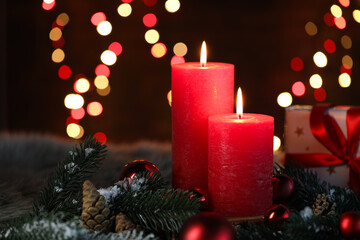 Burning candles, fir tree branches, cones and baubles against black background with blurred lights, closeup with space for text. Christmas greeting card