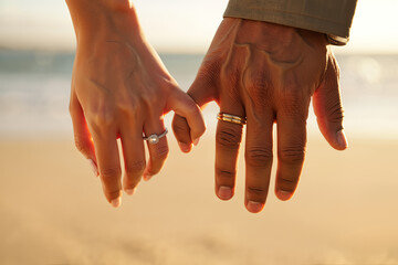 Close-up of an engaged couple holding hands with diamond and wedding rings visible in warm golden sunlight on a beach, representing deep love and commitment.