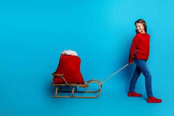 Girl pulls a sled with a red santa sack in a festive christmas scene against a bright blue...