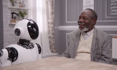 Elderly happy black man chatting with a friendly robot in a modern home, symbolizing innovation and connection