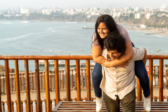 Young couple enjoying piggyback ride at city viewpoint - Powered by Adobe