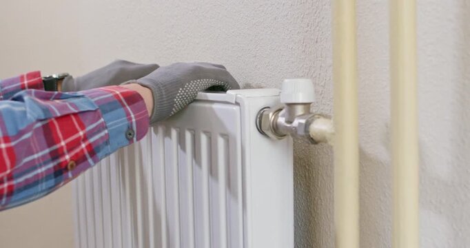 Plumber grips radiator sides checking bracket rigidity before new parts installation. Worker tests mount strength ensuring panel stays level during heating service