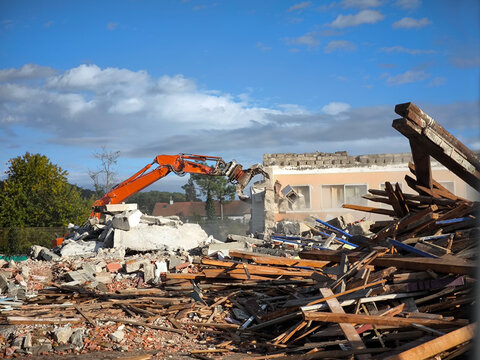 Escavadora de bra&ccedil;o longo em a&ccedil;&atilde;o no desmantelamento de um edif&iacute;cio. A m&aacute;quina est&aacute; sobre uma grande pilha de escombros incluindo t&aacute;buas de madeira quebradas, tijolos e peda&ccedil;os de concreto
