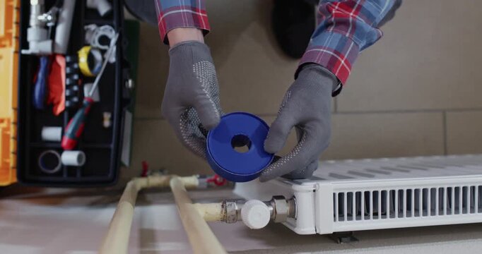 Installer opens PTFE tape pack near radiator while preparing sealing. Skilled plumber wraps tape on male thread and stretches evenly trying to cover crest upper view