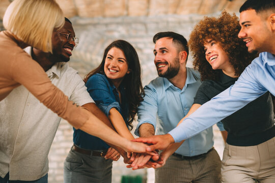 Diverse, multi-ethnic business team stacking hands in the center, showing unity, teamwork, and success in a modern office