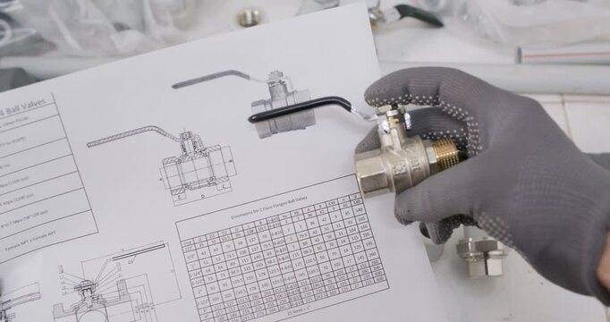 Technician holds brass ball valve reviewing datasheet drawing. Professional plumber matches port size and thread spec noting pressure rating with torque value