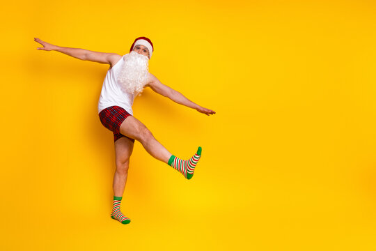 Joyful santa in pajama jumps against bright yellow background creating a funny festive home scene for holiday marketing