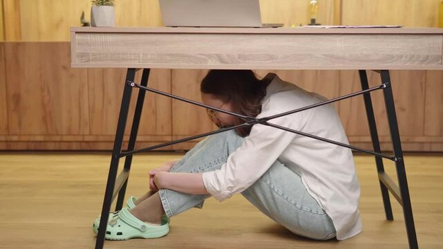 Stressed Woman Hiding Under Desk from Fear or Anxiety