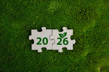 Wooden puzzle pieces with numbers 2026 and green leaf symbols, representing growth, sustainability, and future planning on green moss background