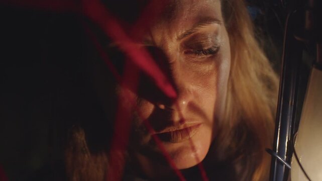 Portrait of a woman whose face is illuminated by the flickering flame of a kerosene lamp against the background of red threads in the dark