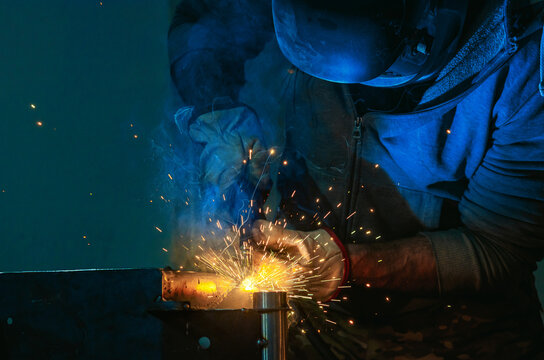 Welding shop worker in protective helmet and gloves. Blue light of welding work with bright sparks.