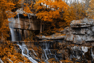 Fototapeta premium Autumn waterfall over granite ledges with golden leaves and reflection