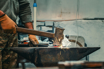 Hands of craftsman in gloves with iron hammer align iron part on stone. Preparation for welding work
