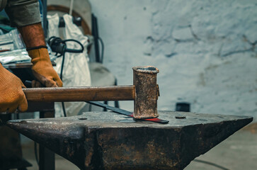 Hands of craftsman in gloves with iron hammer align iron part on stone. Preparation for welding work