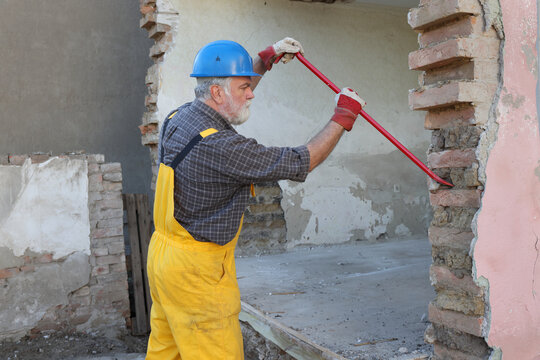 Worker demolishing old building wall using crowbar tool