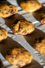 Close-up of raw cookie dough with chocolate pieces placed on parchment paper before baking. Homemade dessert preparation in natural light, concept of sweet food and cooking process.