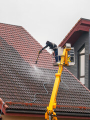Professional worker cleaning roof tiles with high-pressure washer from yellow lift platform