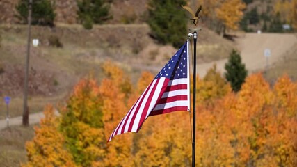 American flag in Cripple Creek, Colorado blowing in gentle breeze with historic mine in the background and fall colors in the foreground. - Powered by Adobe