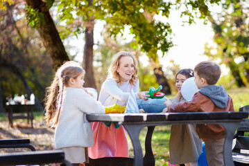 Female animator playing with a group of children at an outdoor birthday party at a table.