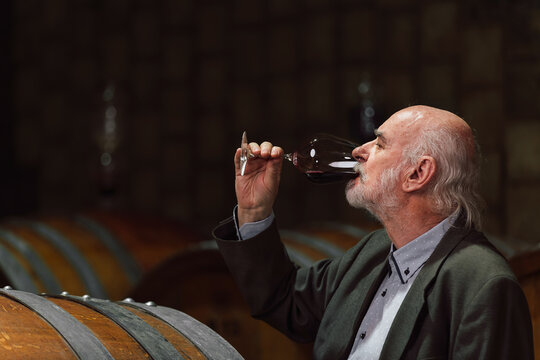 A man savors a glass of red wine, surrounded by wooden barrels in a cozy winery, enjoying the rich flavors.