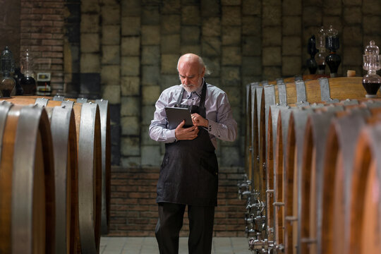 A winery expert inspects data on a tablet while surrounded by oak barrels. The atmosphere is quiet and focused.