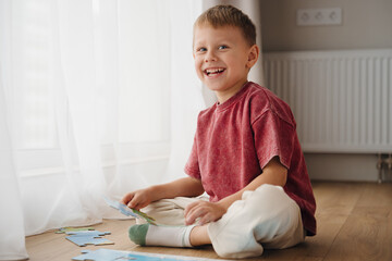 Naklejka premium A happy child sits on the floor of a warm living room, focused on a colorful puzzle in front of him. Sunlight streams in through the window, creating a cheerful atmosphere.