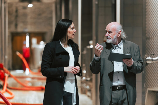 Two people discuss brewing techniques in a modern brewery. The guide explains while showcasing equipment and processes.