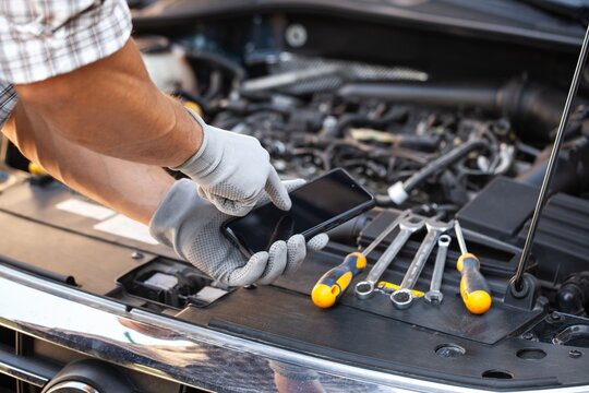 A auto mechanic hands repair auto with mobil phone - Powered by Adobe