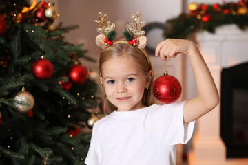 Little girl with ornament near Christmas tree at home