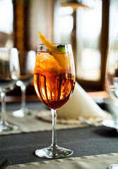 Glass of orange cocktail with ice, citrus peel and mint on restaurant table, bright Aperol spritz.