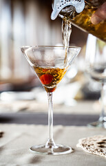 Bartender pouring cocktail into a martini glass with cherry garnish, elegant drink preparation close-up.