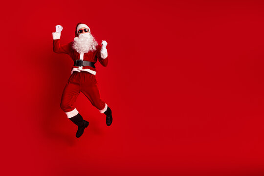 Santa jumps in a red costume with hat belt and beard against a bold red background for Christmas celebration and festive holiday magic